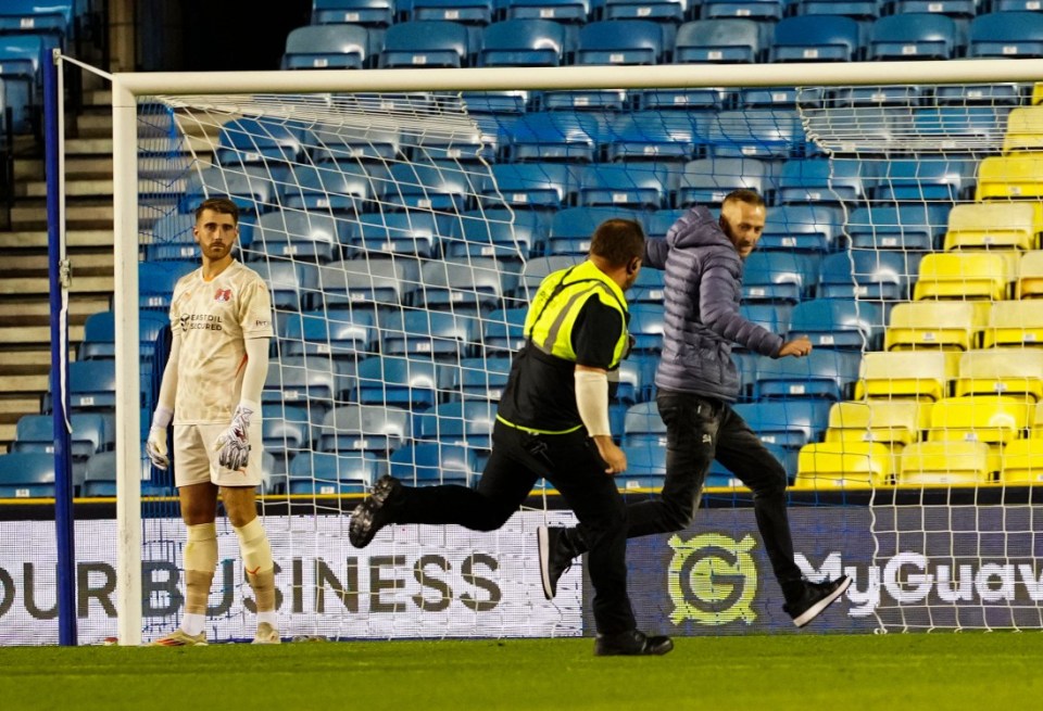 Shocking moment Carabao Cup clash suspended as idiot pitch invader restrained by goalkeeping coach and carried away